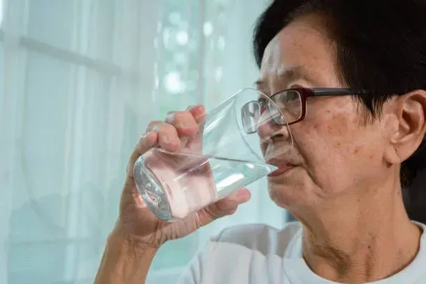 An elderly woman is drinking a glass of water.