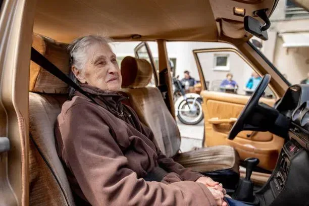 An elderly woman is sitting in the driver 's seat of a car.