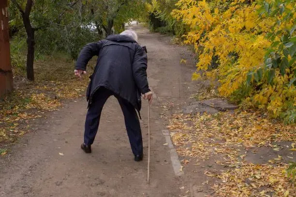 An elderly man is walking down a path with a cane.