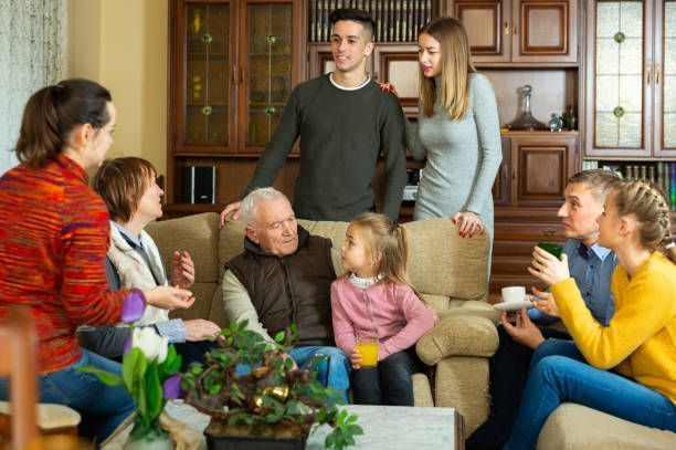 A large family is sitting on a couch in a living room talking to each other.
