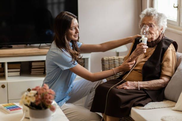 Caregiver assisting elderly person with a nebulizer in a home setting.
