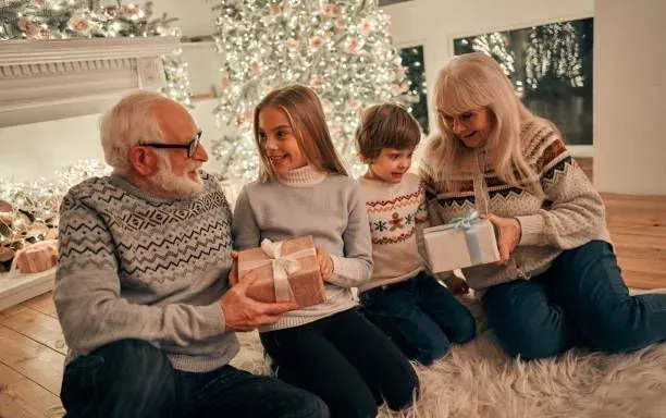 A family is sitting on the floor in front of a christmas tree holding gifts.