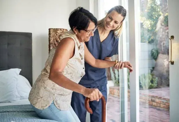 A nurse is helping a woman with a cane to get out of bed.