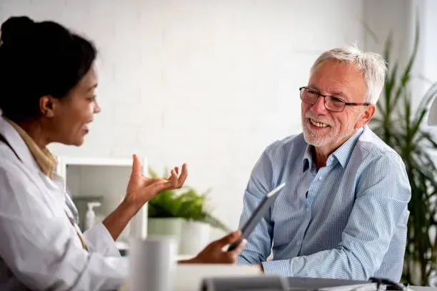 A doctor is talking to an older man who is sitting at a desk.