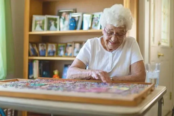 An elderly woman is sitting at a table playing a puzzle.