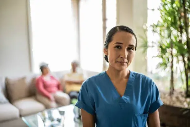 A nurse in a blue scrub is standing in a living room.