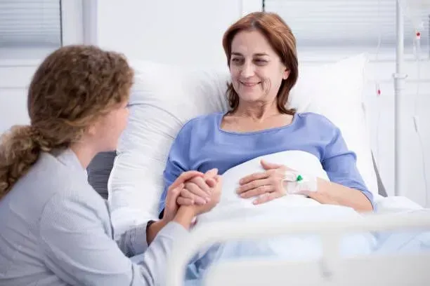 A woman is holding the hand of a patient in a hospital bed.