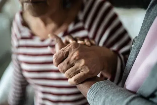 A man is holding the hand of an elderly woman.