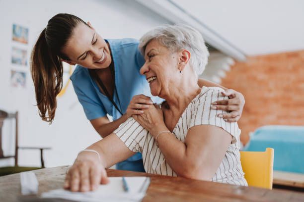 A nurse is hugging an elderly woman who is sitting at a table.