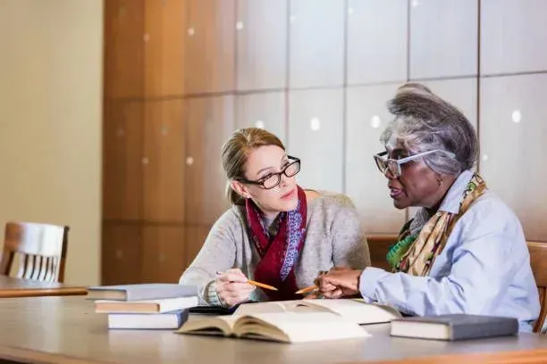 Two women are sitting at a table reading books.