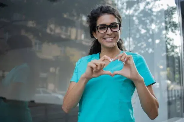 A nurse is making a heart shape with her hands.