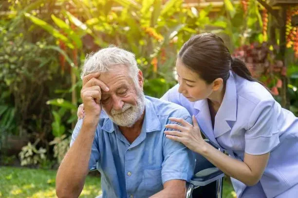 A nurse is comforting an elderly man in a wheelchair.