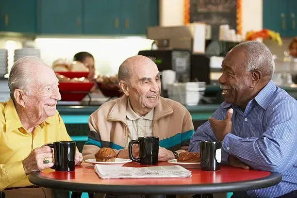 Three older men are sitting at a table drinking coffee and talking.