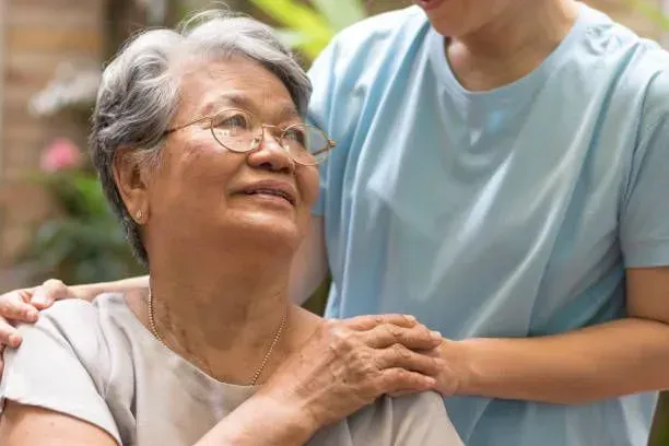 A woman is standing next to an older woman in a wheelchair.