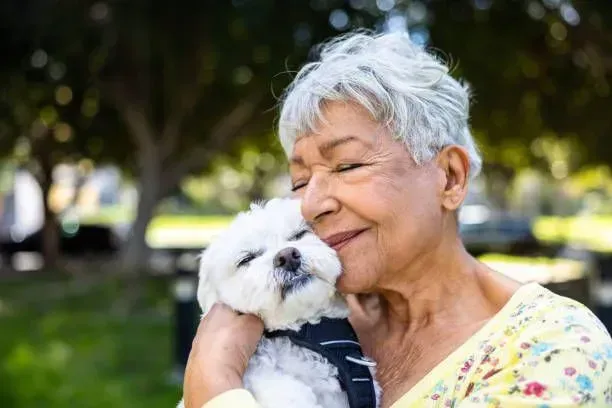 An elderly woman is holding a small white dog in her arms.