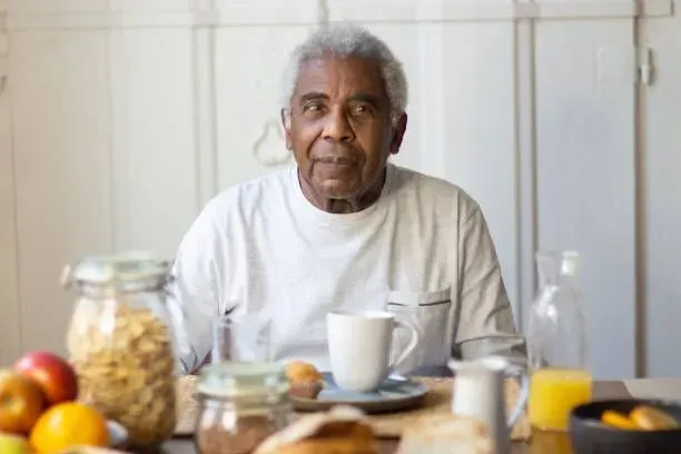 An elderly man is sitting at a table eating breakfast.