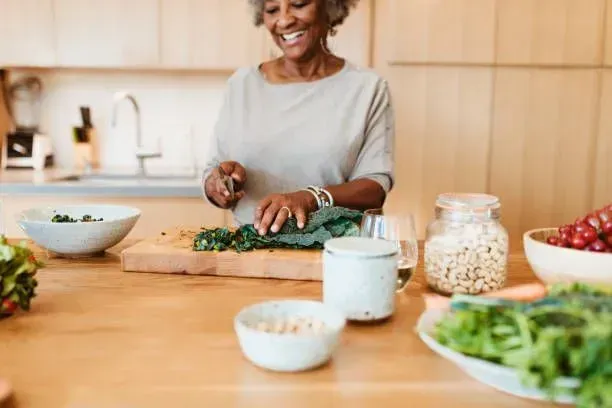 A woman is cutting vegetables on a cutting board in a kitchen.