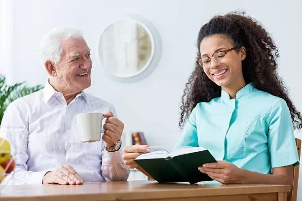 A nurse is reading a book to an elderly man.