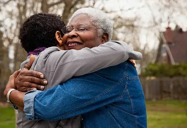 An older woman is hugging a younger man in a park.
