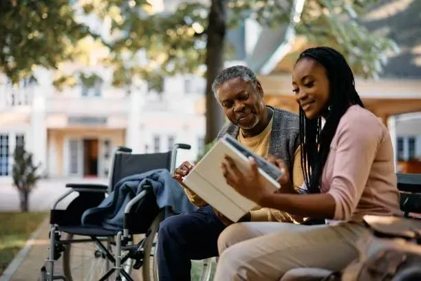 A woman is reading a book to an older man in a wheelchair.