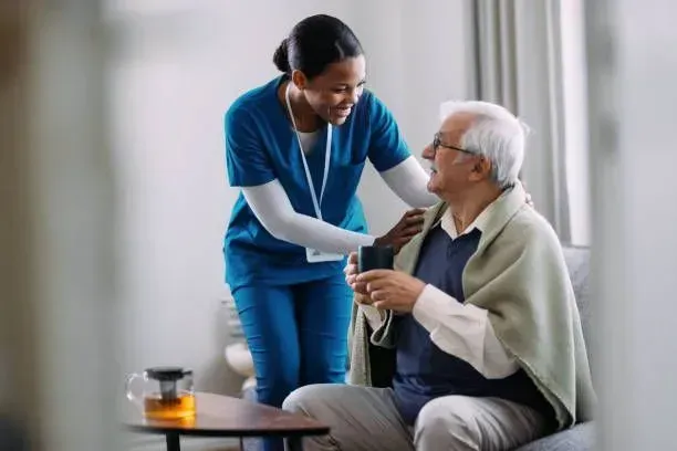 A nurse is helping an elderly man drink from a cup.