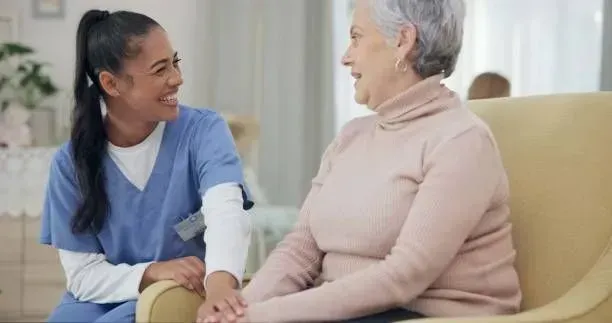 A nurse is holding the hand of an elderly woman while sitting on a couch.