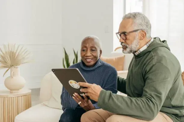 A man and a woman are sitting on a couch looking at a tablet.
