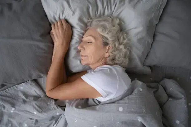 An elderly woman is sleeping in a bed with a pillow.