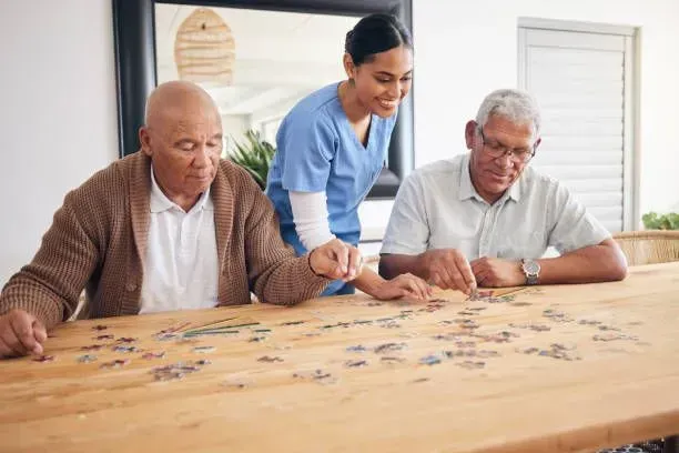 A nurse is helping two elderly men do a puzzle.