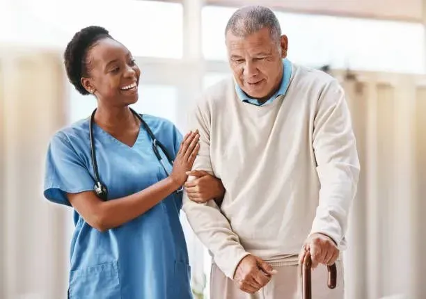A nurse is helping an elderly man walk with a cane.
