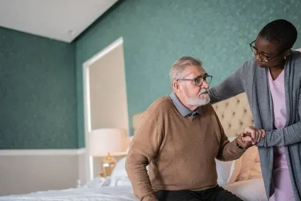 A nurse is helping an elderly man sit on a bed.
