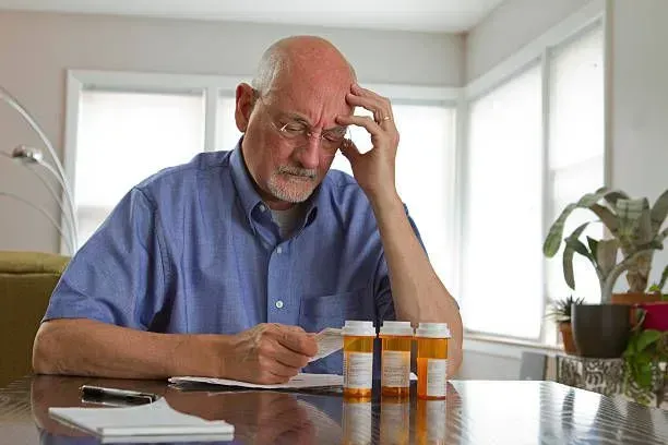 An older man is sitting at a table looking at his prescriptions.