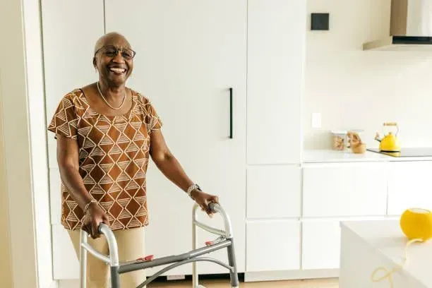 An elderly woman is using a walker in a kitchen.