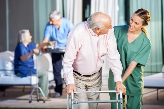 An elderly man with a walker is being helped by a nurse.