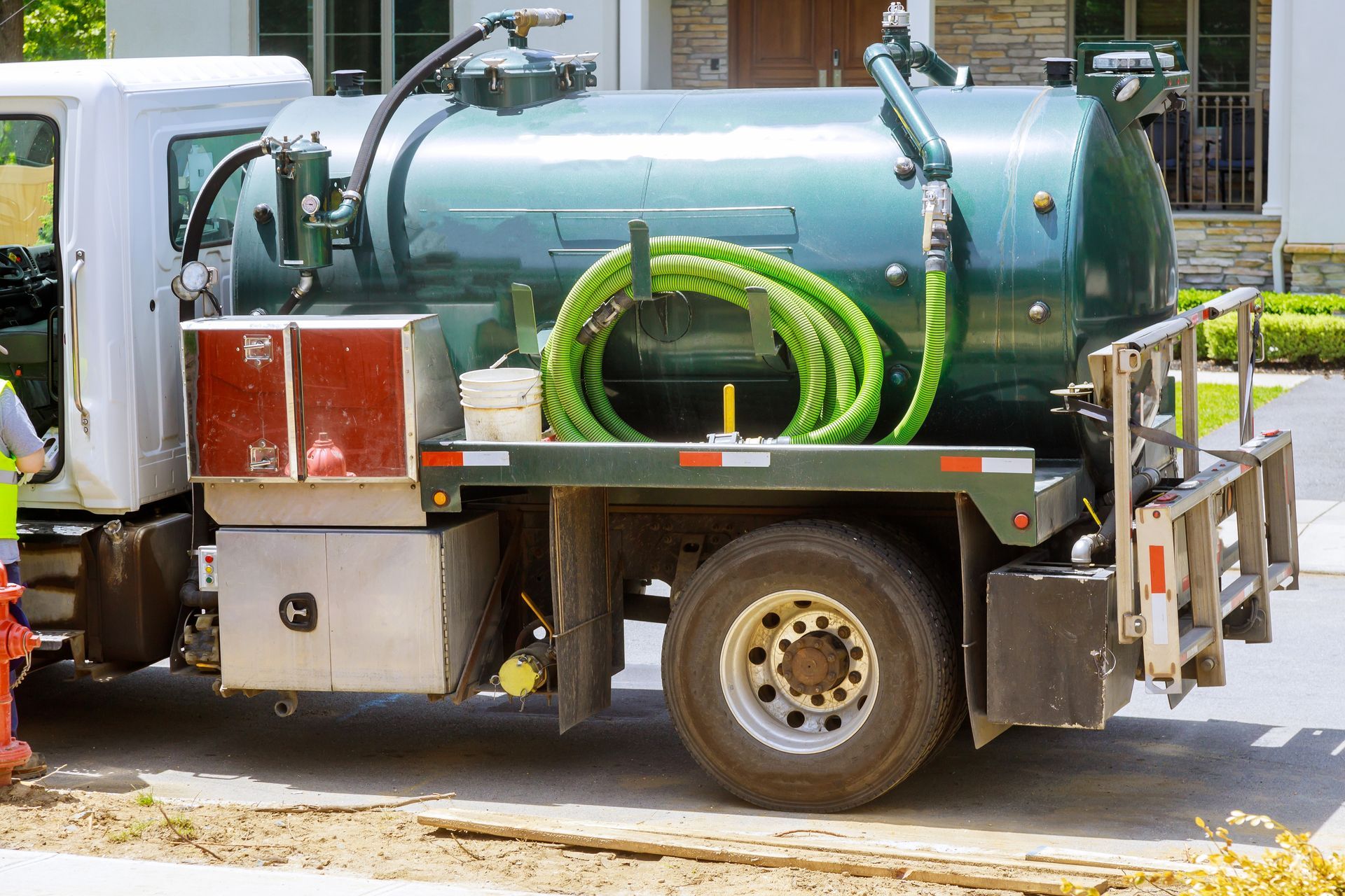 septic pumping truck servicing residential tank with hoses connected in a rural property driveway