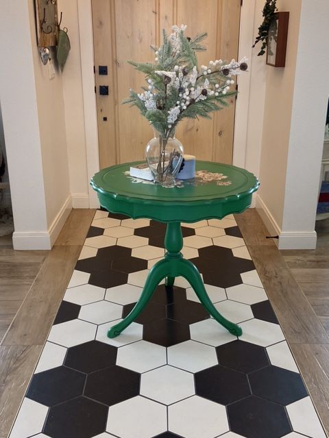 Green table with a floral arrangement in a hallway with geometric tile flooring.