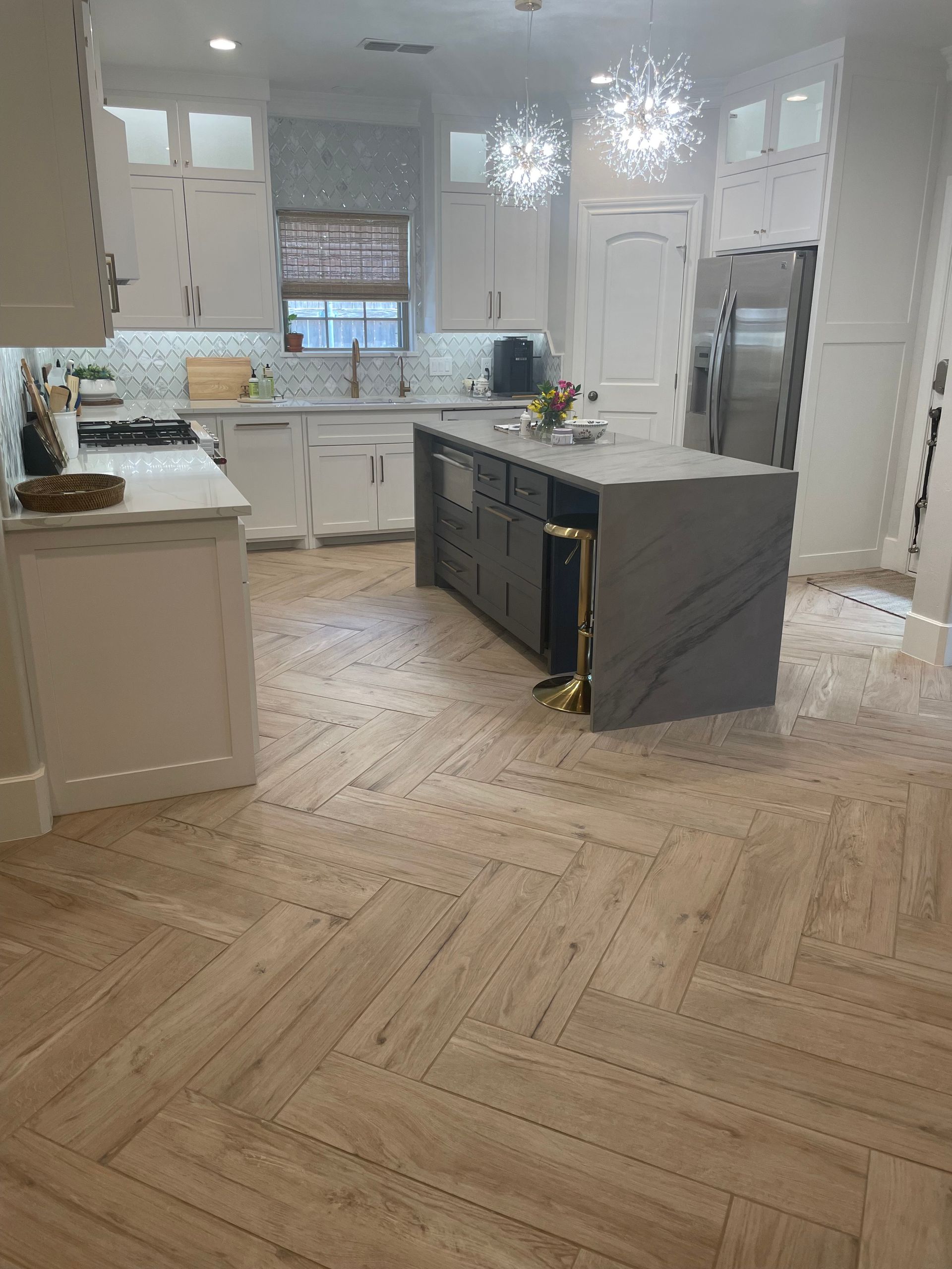 Kitchen with white cabinets, gray island, and herringbone wood-look tile flooring. Kitchen with white cabinets, gray island, and herringbone wood-look tile flooring.