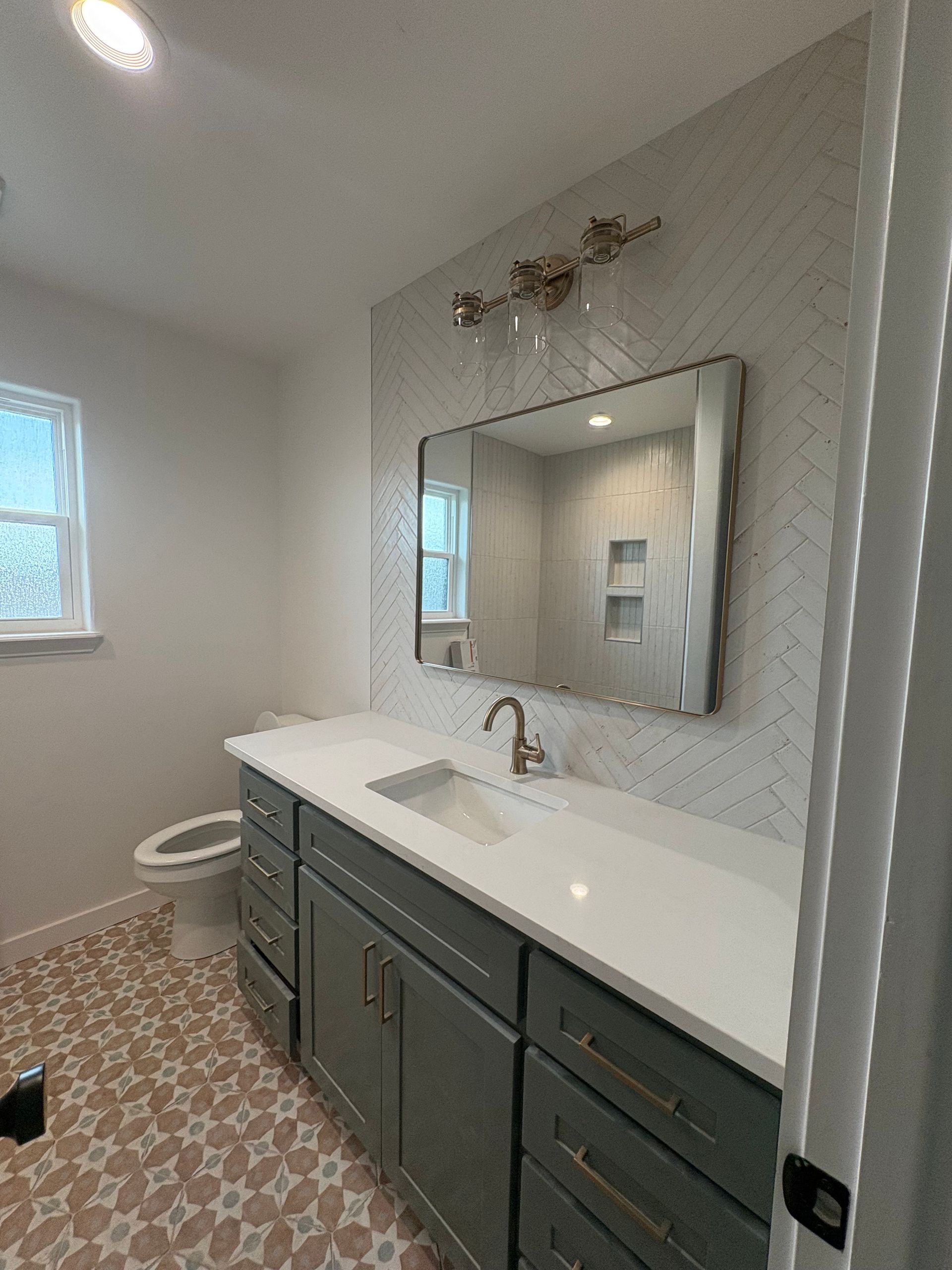 Modern bathroom with gray vanity, white countertop, patterned floor, and large mirror.