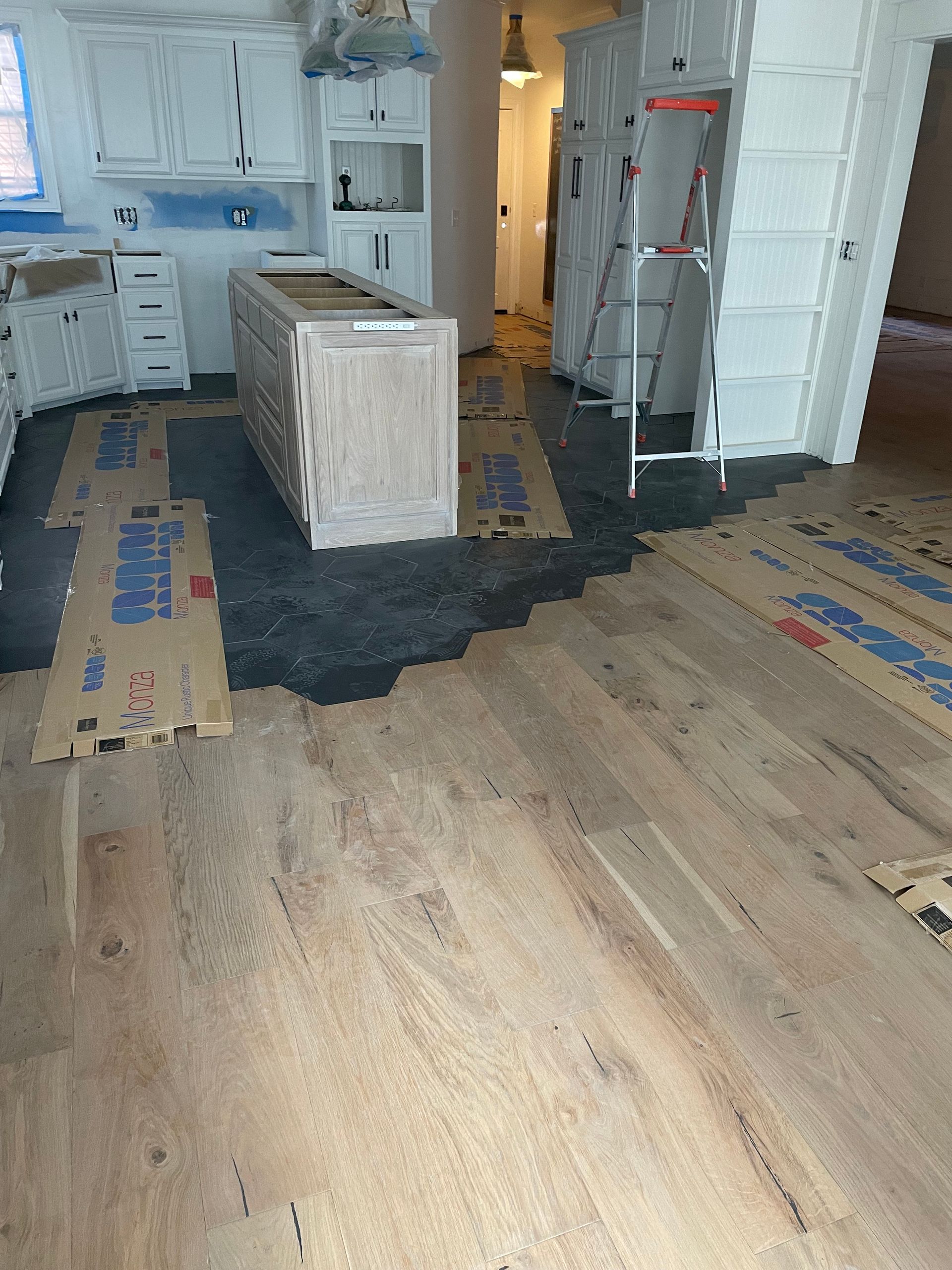 Wooden floor being installed in a kitchen. Cabinets and island are present; areas are protected with cardboard. Wooden floor being installed in a kitchen. Cabinets and island are present; areas are protected with cardboard.