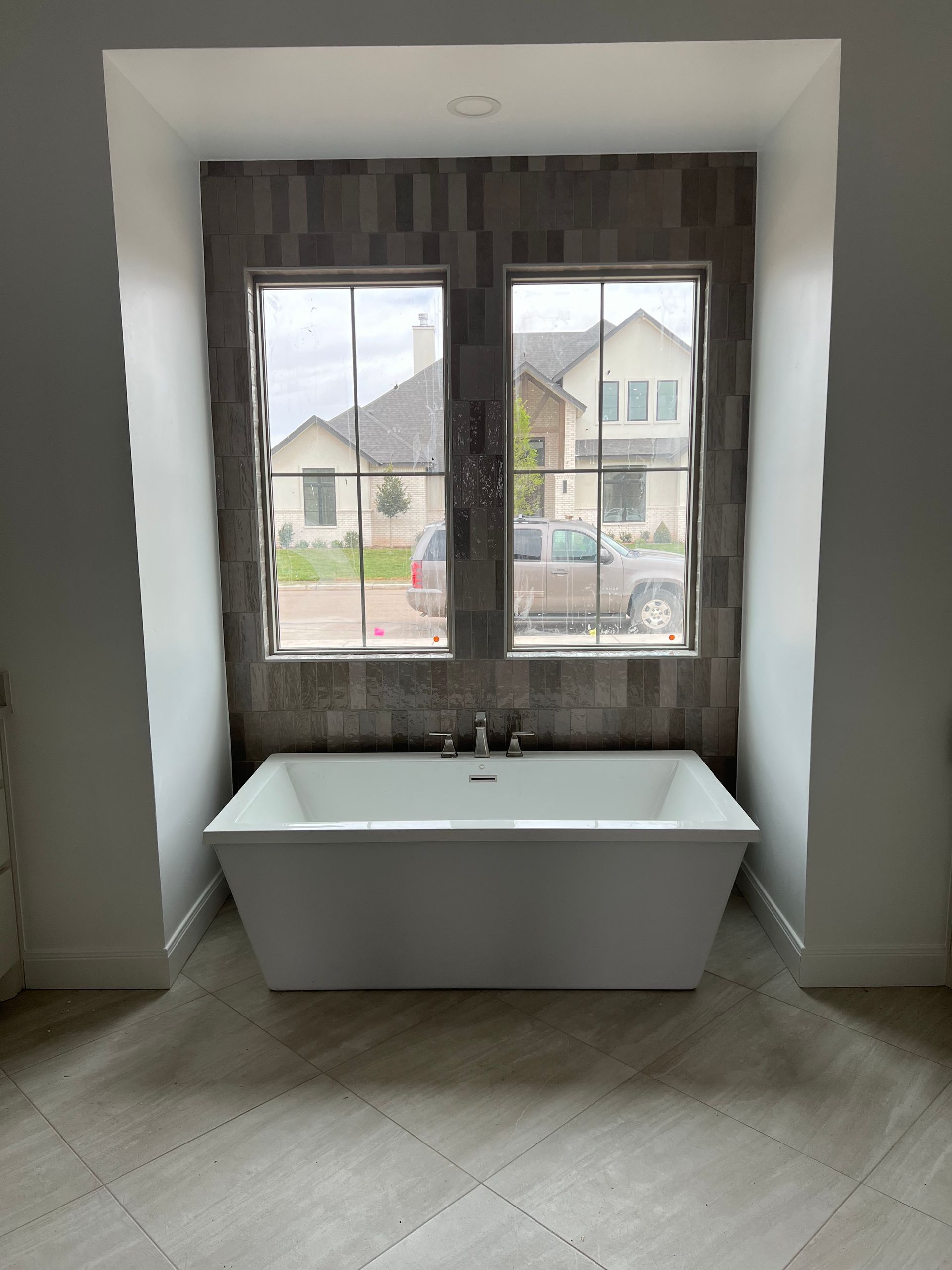 Freestanding white bathtub under two windows with gray tile backdrop. Freestanding white bathtub under two windows with gray tile backdrop.