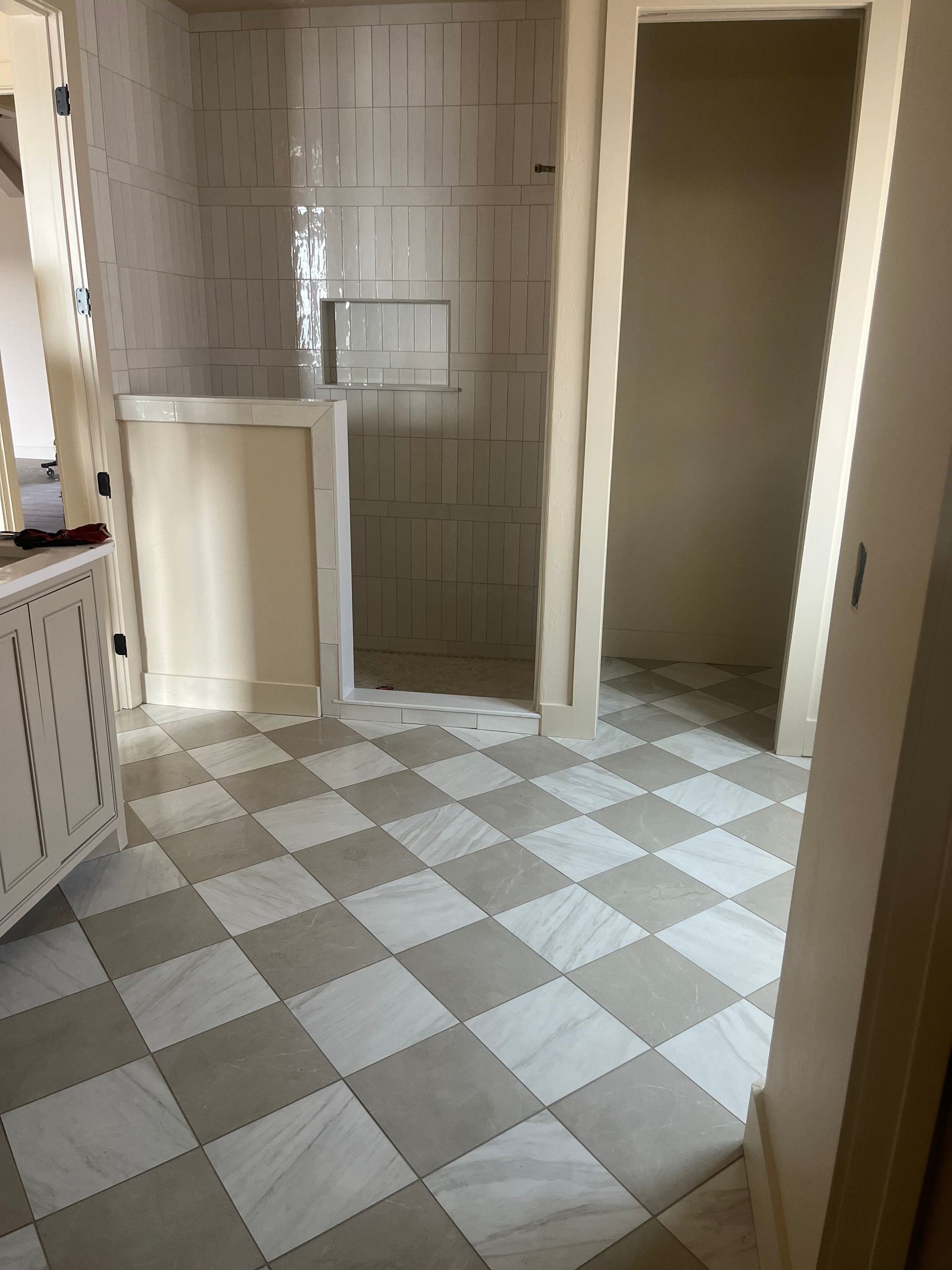 Bathroom with checkered floor, neutral walls, and shower area. Open doorway on right. Bathroom with checkered floor, neutral walls, and shower area. Open doorway on right.