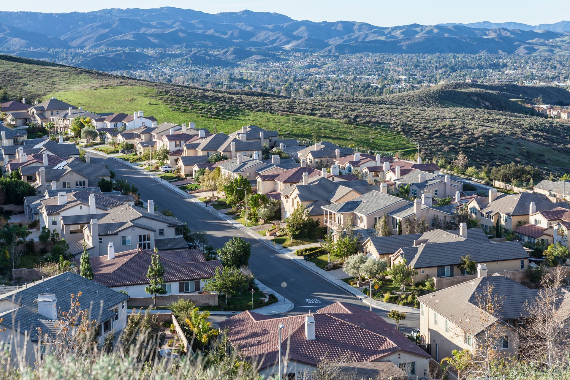 Suburban hillside homes overlooking a sprawling valley and distant mountains under a clear sky