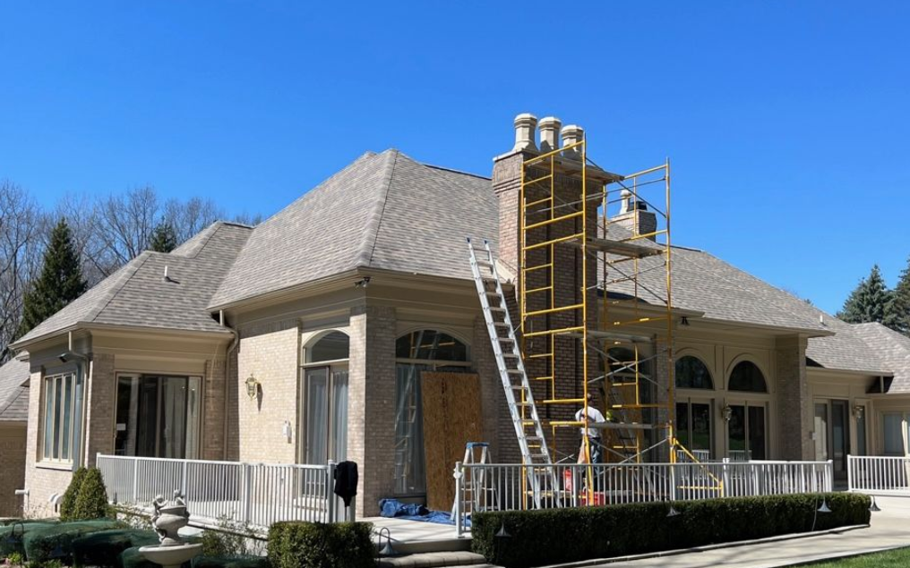 House exterior with workers and scaffolding during roof construction under a blue sky
