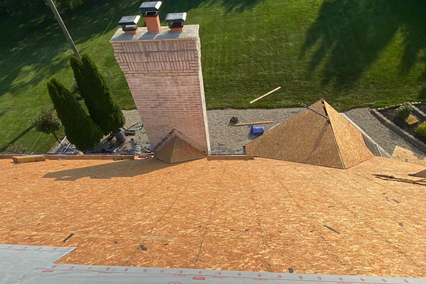 A roof during shingle replacement, a brick chimney, and green lawn below