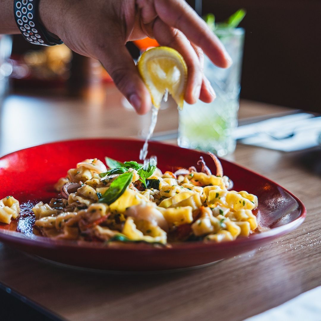 a person is squeezing a lemon over a plate of pasta