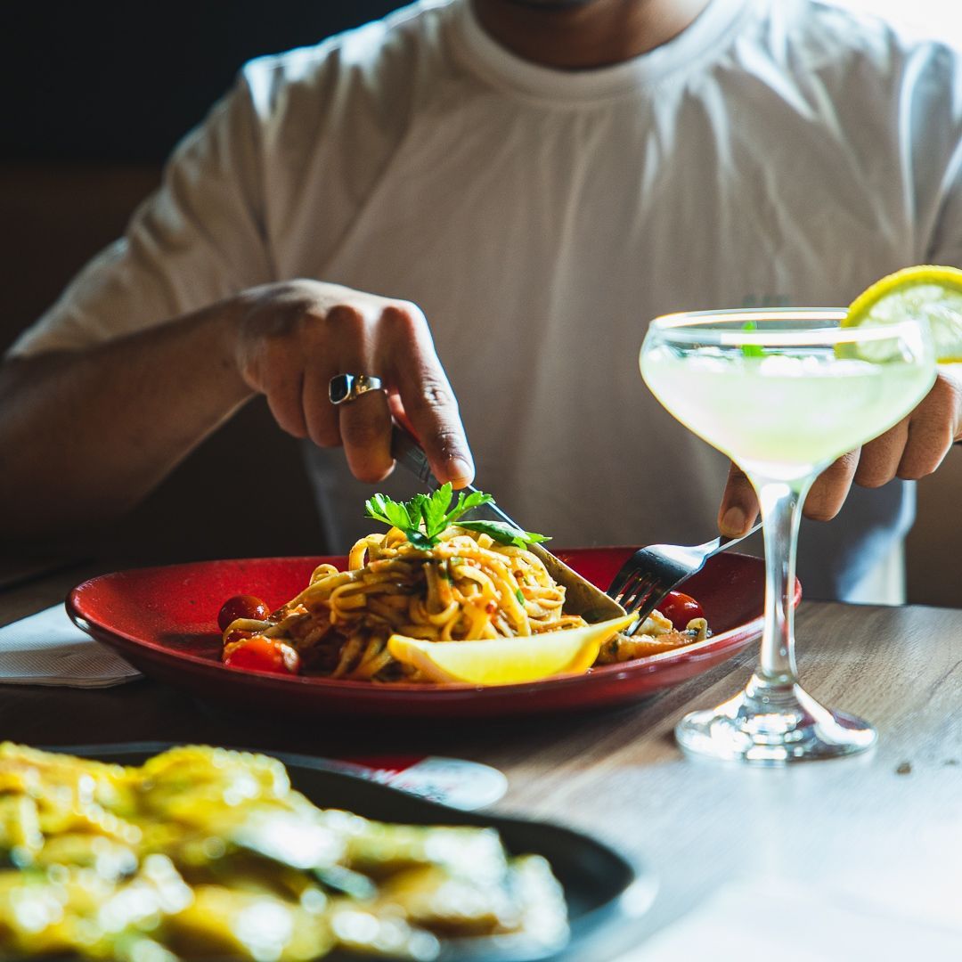 an Italian man is eating spaghetti with a martini in the background