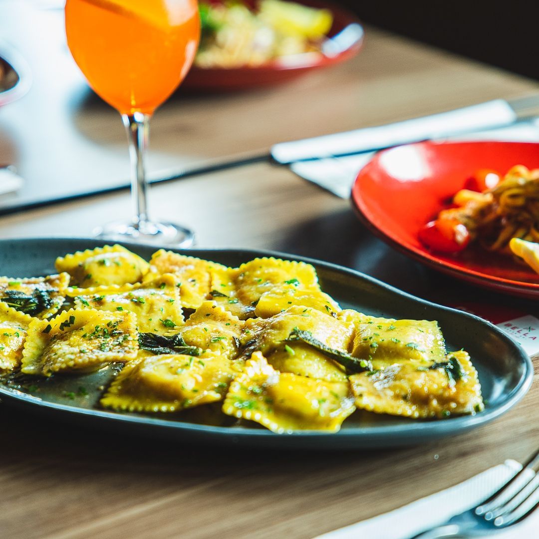 a plate of ravioli sits on a table next to a glass of orange juice