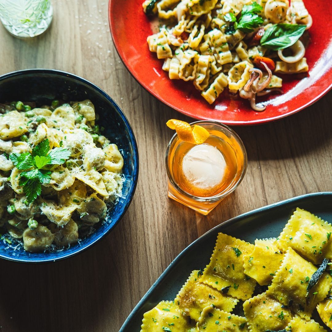 a bowl of Italian pasta sits next to a plate of ravioli