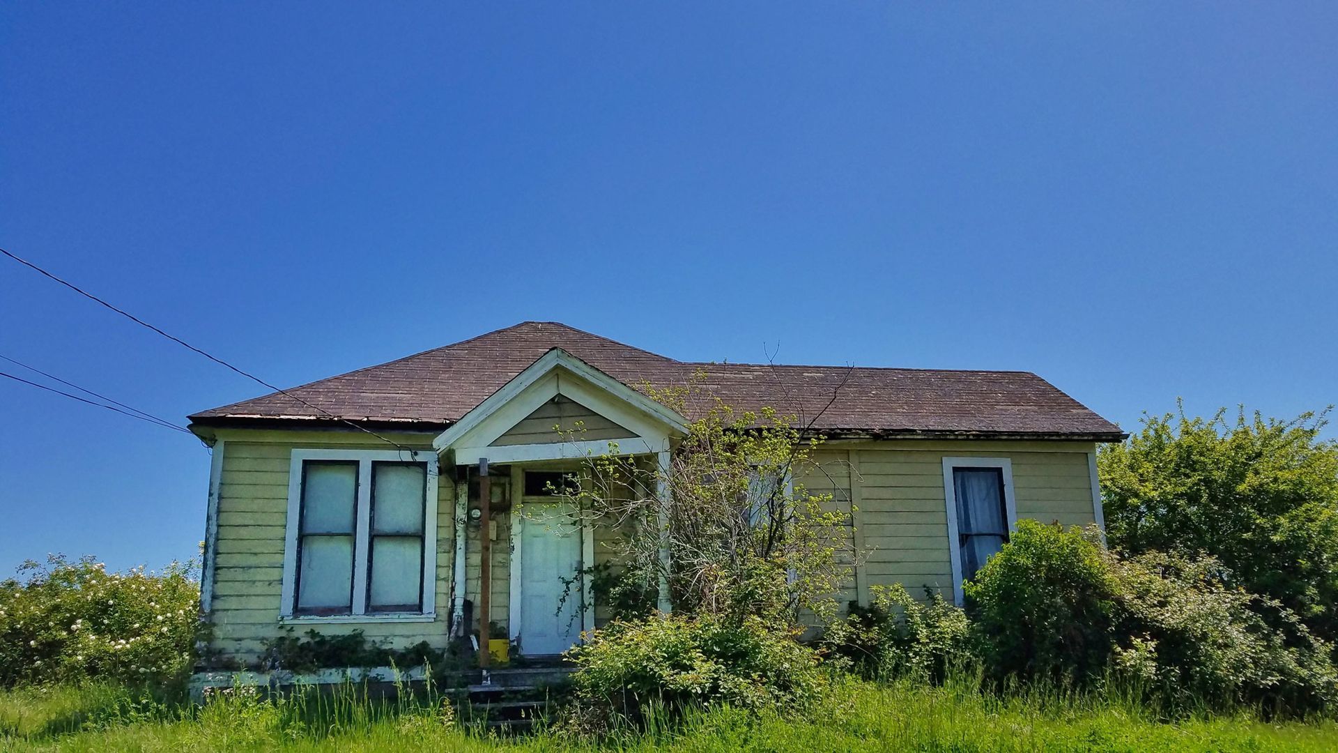 An old yellow house with a red roof is sitting in the middle of a grassy field.