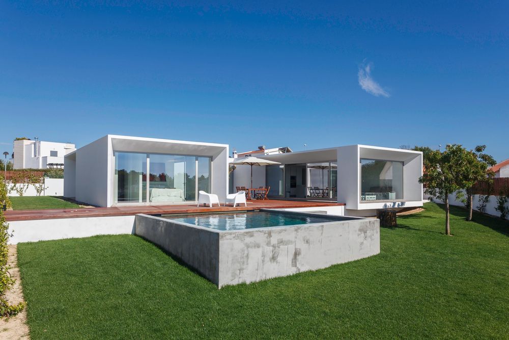 Casa moderna bianca con piscina e prato verde sotto un cielo azzurro limpido.